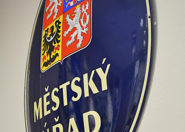Tmavě modrý jednostranně smaltovaný ovál s velkým státním znakem ČR a nápisem OBECNÍ ÚŘAD