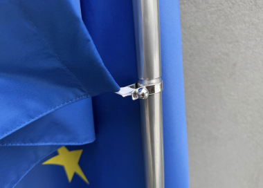 Detail uchycení interiérové tištěné vlajky pomocí poutek na stojanu.